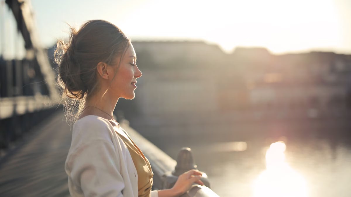 A young woman stands on a bridge enjoying the warm sunset over the city skyline.